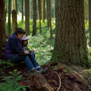 child sitting at base of tree in forest