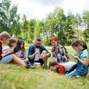 Young students with pencils and notepads outside with two adults, fieldwork.