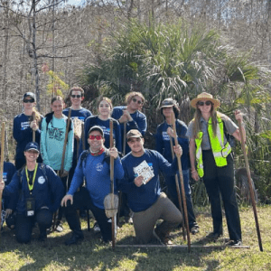 A group of Junior SeaKeepers posing in a grassy field with leafless trees behind them