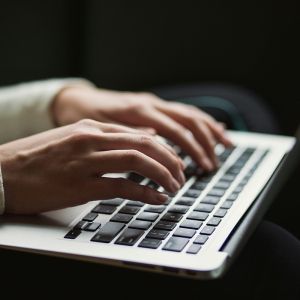 A person's hands hover over a laptop keyboard.