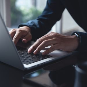 Two hands type on a laptop keyboard