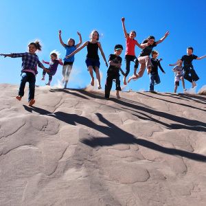 A group of kids jumping on a sand dune
