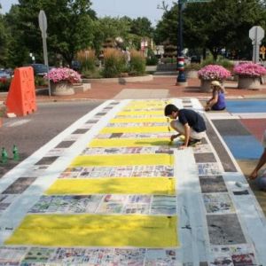 Photo of a group of four children kneeling or sitting while painting over a street