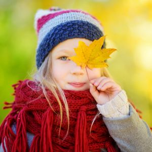 young girl holding a yellow autumn leaf in front of her eye
