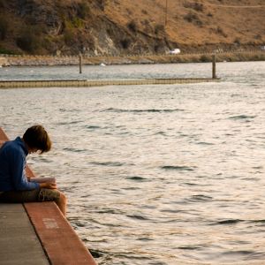 Middle school student sitting at lakeshore reading book 