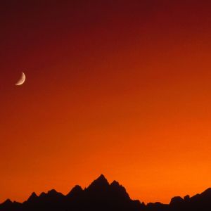 Reddish sky, moon, silhouette of mountains.