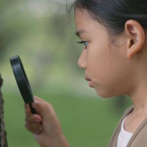Young girl holding a magnifying glass to look at tree bark
