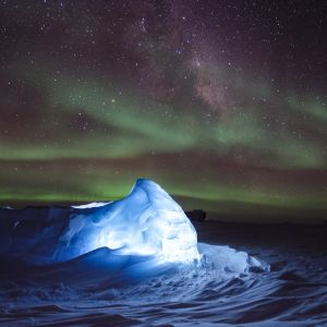 Illuminated ice shines bright in white and blue. Stars dance with green as the Northern Lights twinkle above. 
