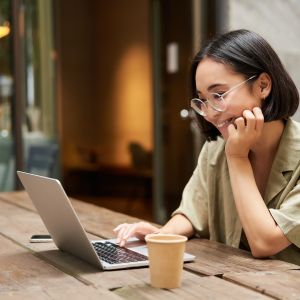 A woman with short hair and wearing glasses, smiles while looking at her laptop