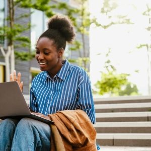 Person holding video conference with laptop and waving while sitting on stairs outdoor