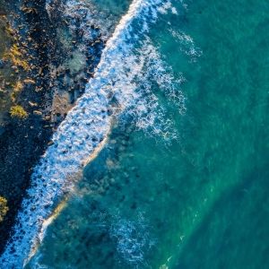 A breathtaking aerial view showcasing turquoise ocean waves crashing against a rocky shoreline.