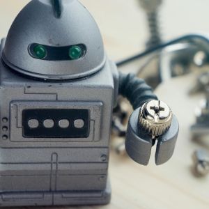 A robot toy holding a screw with various metal parts blurred behind it