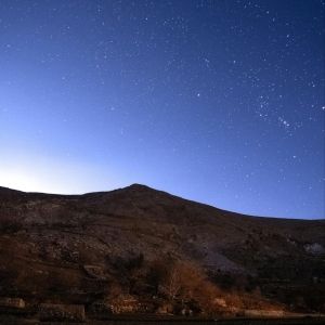 A night sky with stars and a hill in front of it
