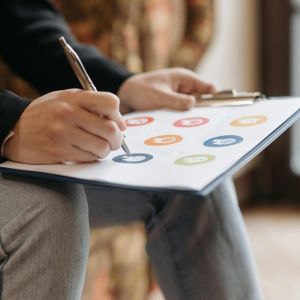 Up-close of a clipboard with paper that has icons on it, being marked by a pen.