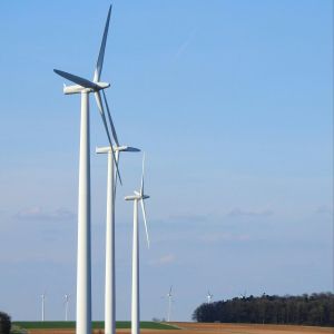 Three wind turbines lined up in a green field with a blue sky behind them