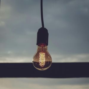 A lightbulb hanging from the ceiling in front of a window with a blurred city skyline.