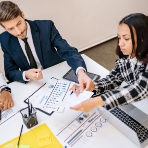 Three people sit around at table with laptops and business documents.