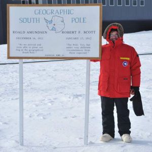 A person stands next to a sign that states "Geographic South Pole"