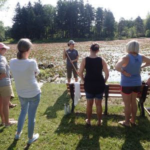 A group of adults stands in a half-circle in front of a wetland listening to an environmental educator 
