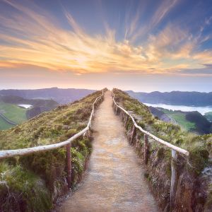 path with railing on mountaintop under sunlit clouds in blue sky