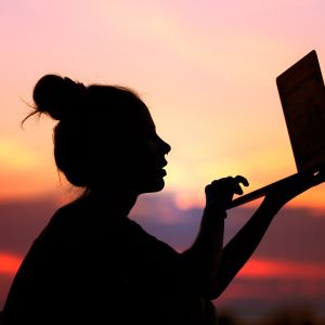 woman holding computer outside at sunset