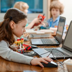 Girl using a laptop while assembling a robot from plastic bricks. 