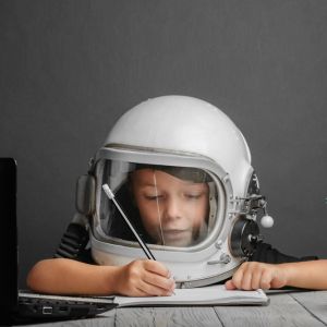 Child wearing an astronaut's helmet and holding a pencil.