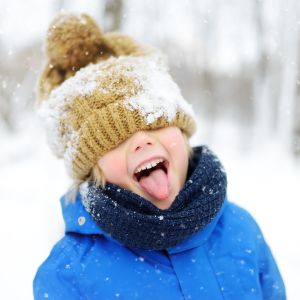 little boy in snow with hat covering eyes and tongue sticking out