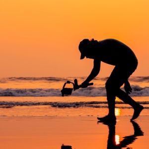 An image of a man on a beach at sunset filming with a handheld camera