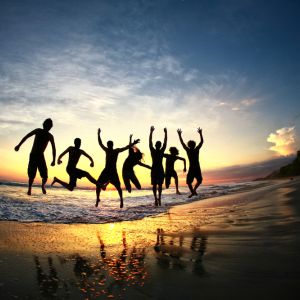 Friends jumping for joy on tropical beach at sunset in a group formation