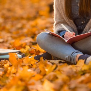 student sitting on autumn leaves writing in notepad
