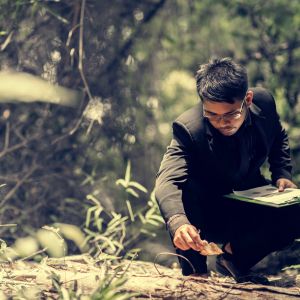 young man studying leaves in forest