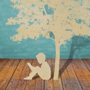 white paper cutout of tree and boy sitting under it reading while sitting on hardwood floor with painted blue background