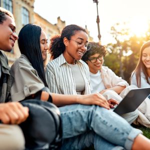 students sitting on grass on campus socializing, studying and spending time at leisure. 
