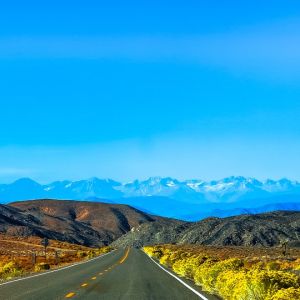 A highway road leading away from the viewer to hills and a mountain range in the distance