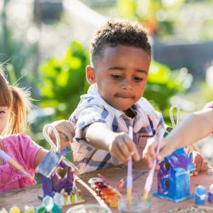 Three kids painting bird houses outside on a sunny day