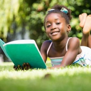 young girl reading book in grass