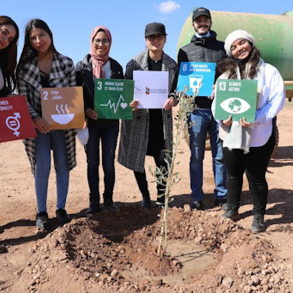 six people stand in a row outside, each holding a square to represent the UN sustainability goals