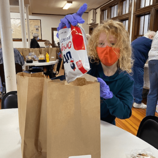 Child wearing face mask and gloves helps to bag food to hand out at the food pantry. 
