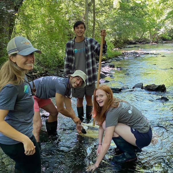 Summer training for four Difference Maker Mentors smiling while they stand in a forest creek. 