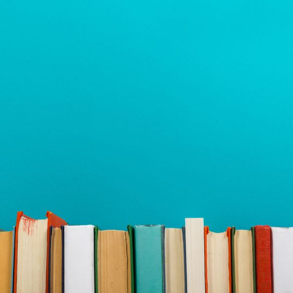 A row of multicolor books run along the bottom of the photo with a bright teal wall above them. 