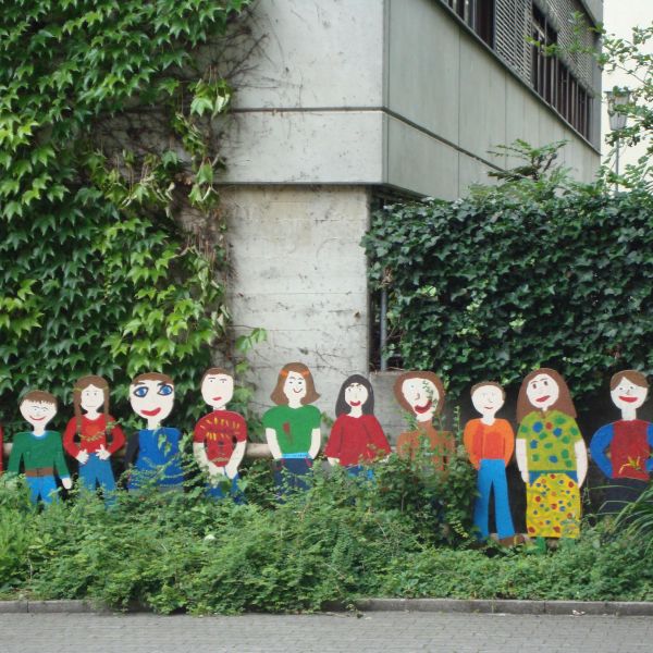 Background is an ivy-covered building and lined up in front of the building are paper cutouts of smiling people