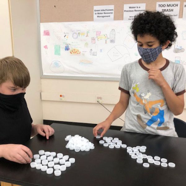 Three masked students count and sort bottle caps during afterschool program.