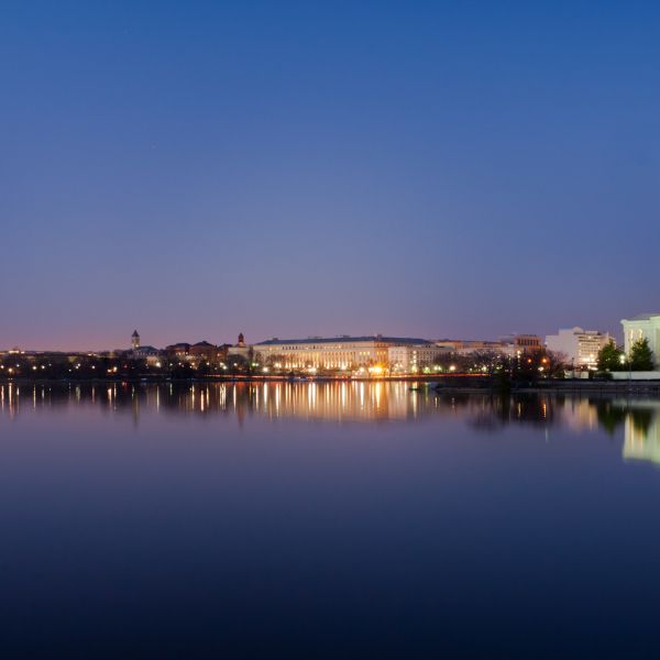 Washington, DC. at night. The Washington Monument and Jefferson Monuments are illuminated in a warm glow and their reflections bounce of the water. 