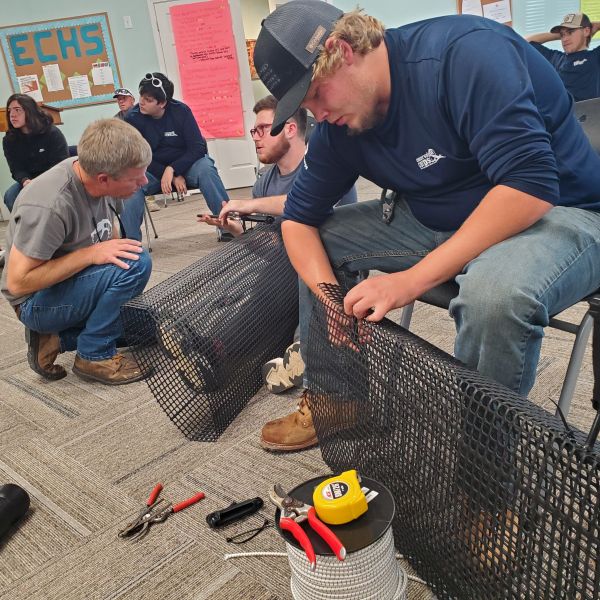 A group of students build black mesh cages in an indoor room.
