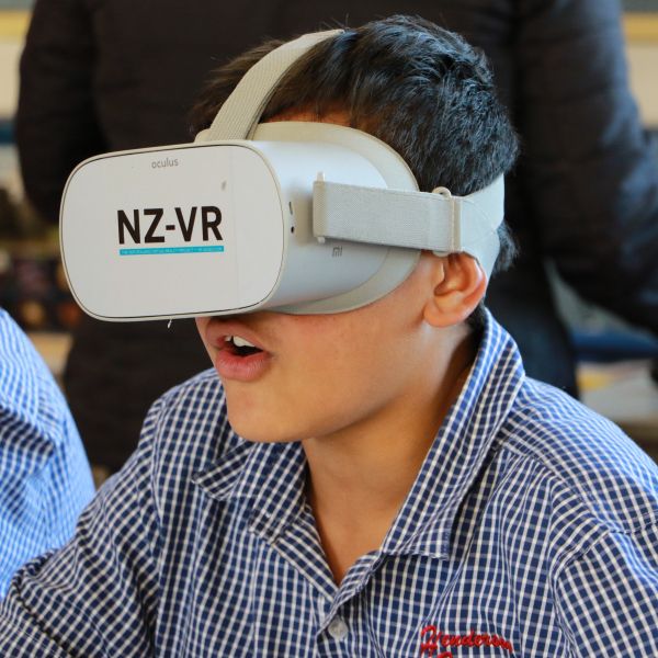 a young student sitting at a desk wearing a white VR headset with NZ-VR on it