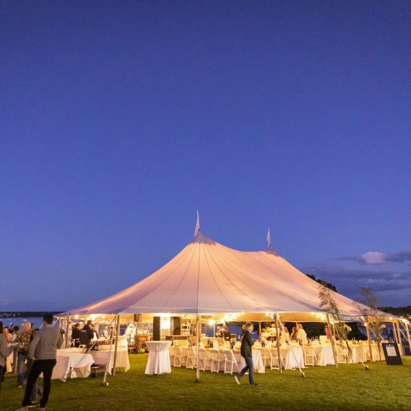 A brightly lit outdoor tent on grassy field under a partly cloudy evening sky
