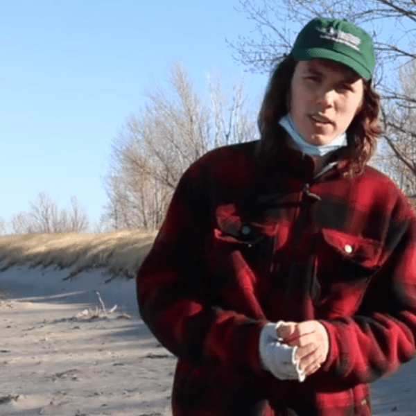 Screenshot of a person outside near a ridge of sand dunes.