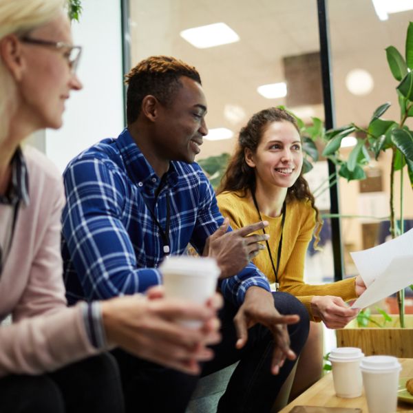 three people wearing conference badges, talking in lounge, coffee on table