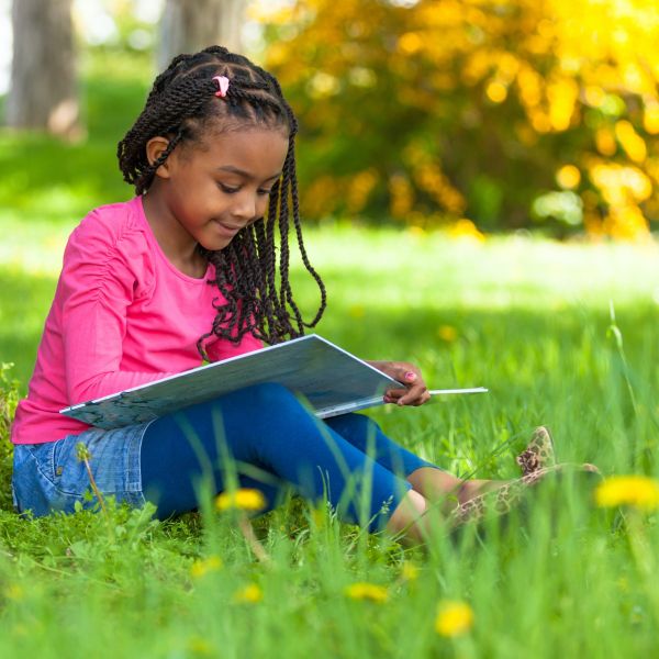 young girl reading book outside fall leaves on tree